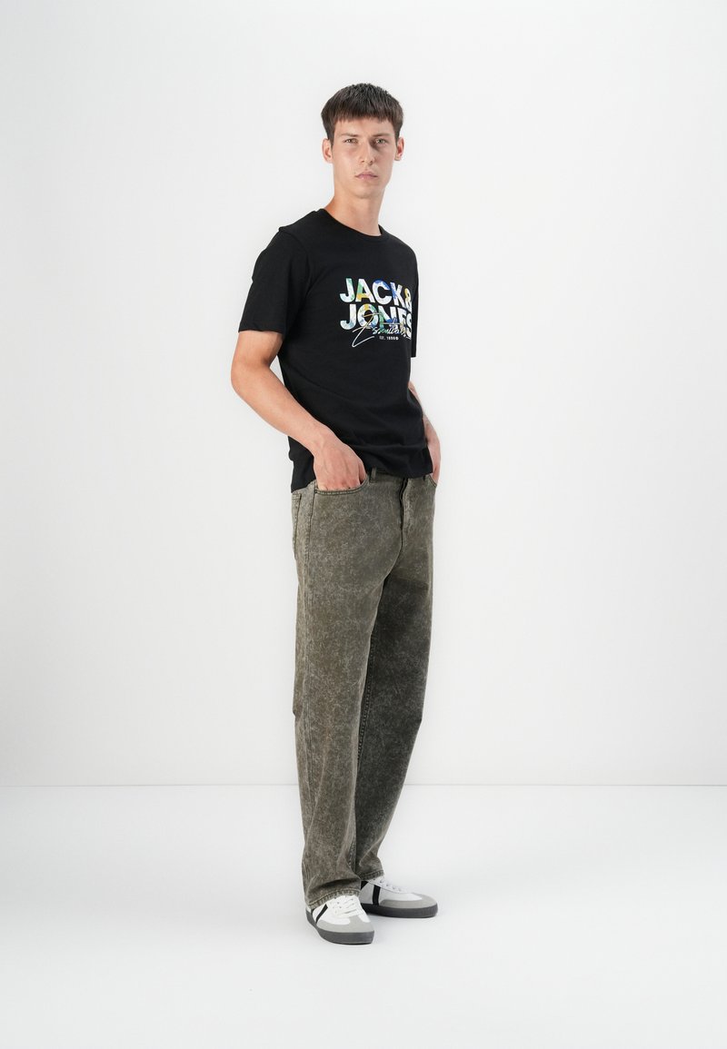 Black T-shirt with colorful "JACK & JONES" logo, paired with olive green pants. White sneakers complete the outfit. Simple design, casual look.