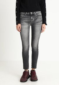 Jeans neri slim-fit con finitura invecchiata, design a cinque tasche e cuciture bianche a contrasto, abbinati a sneaker bordeaux.