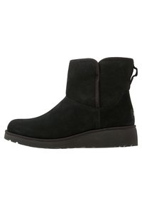 Botas de tobillo de ante negro con punta redondeada, tacón bajo en cuña, costuras laterales y una pestaña trasera para facilitara su colocación. Textura suave y mate.