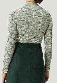 Teksturoitu, poimutettu pitkähihaine paita vihreissä ja vaaleanruskeissa sävyissä, yhdistettynä tummanvihreään tekosuedehameeseen, jossa on vyötärönauha ja sivuhalkio.