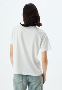 Hvid bomulds t-shirt med korte ærmer og rund hals, vist bagfra. Kombinationen med lyseblå denim jeans.