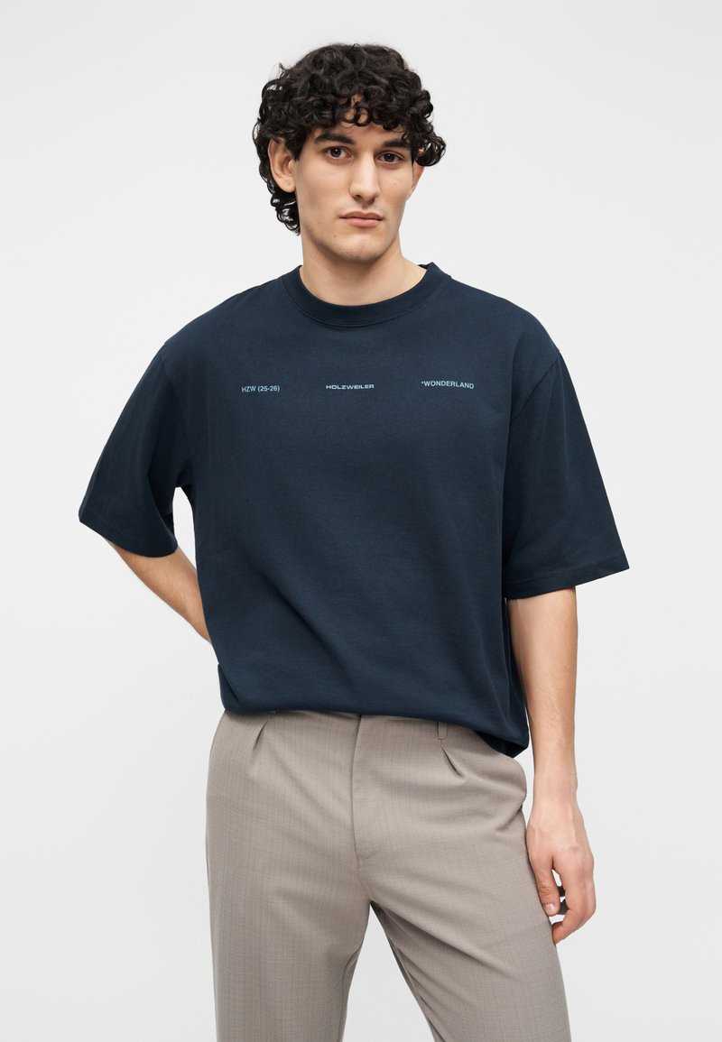 Mörkblå bomulls-t-shirt med korta ärmar och rund halsringning, med vita textdetaljer på framsidan. Mjuk textur.