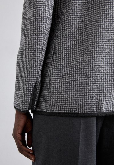 Veste en mélange de laine grise avec un petit motif pied-de-poule, présentant une finition texturée et une coupe sleek, ajustée.