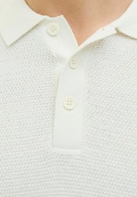 Polo shirt in light beige with a textured knit fabric, featuring a contrasting collar and three white buttons at the placket.
