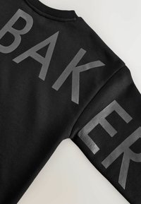 Must jakk, mille rinnal on suured tumehallid tähed "BAK" ja varrukal "ER", valmistatud pehmest kangast.