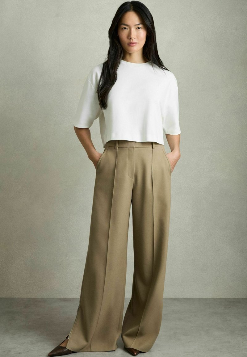 Hvid cropped t-shirt med brede ærmer, parret med højtaljede, beige vide bukser med forfald og sidelukninger.