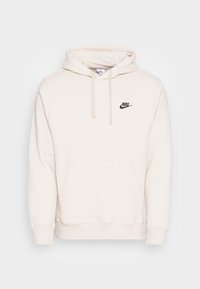 Nike-hoodie i krämfärg, tillverkad av mjukt tyg. Har en framlapp, snörning i huvan och en svart logga på bröstet.
