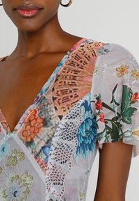 Abito floreale trasparente con scollo a V, motivi multicolori, dettagli in pizzo e maniche corte volanti in un tessuto leggero.