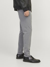 Pantalon gris ajusté en tissu texturé, avec une coupe droite et des ourlets roulés, assorti à des chaussures en cuir noires à lacets.