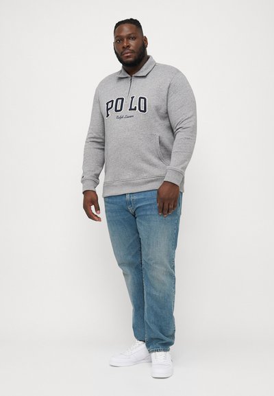 Szürke bolyhos pulóver, cipzárral, melyen tengerészkék "POLO" nyomat és "Ralph Lauren" részletek találhatók. Világoskék farmernadrággal és fehér sportcipővel párosítva.