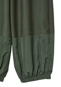 Grüne Hose mit einem strukturierten Oberstoff und einem glatten, glänzenden unteren Abschnitt. Elastische Bündchen an den Knöcheln sorgen für einen gerafften Effekt.
