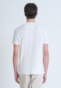 T-shirt bianco a maniche corte con scollo tondo e una leggera texture. Il retro presenta un design pulito e un tessuto morbido. Nessun motivo o accento visibile.
