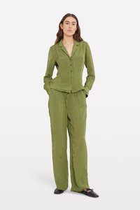 Olive green crinkled fabric outfit featuring a buttoned blazer and loose-fitting trousers, with a structured collar and slip-on black shoes.