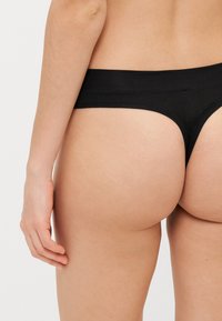 Black thong underwear made of smooth fabric, featuring a low-rise waistband and minimal rear coverage, highlighting a seamless design.