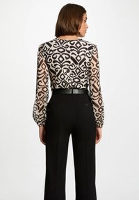 Blusa de patrón transparente en negro y beige, con mangas largas abullonadas y dobladillo elástico. Combinada con pantalones de tiro alto negros y un cinturón.
