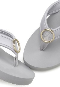 Grijze flip-flops met een matte afwerking, voorzien van een gevoerde band en een gouden cirkelaccent op het kruispunt van de banden.