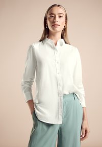 Camisa blanca de botones con mangas largas, cuello estructurado, combinada con pantalones de pierna ancha de color azul claro, mostrando una textura de tela suave.