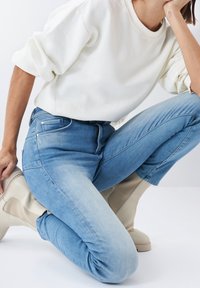 Jeans de denim azul claro con un desvanecimiento gradual, corte ajustado y un bolsillo frontal visible. Combinados con un suéter blanco y botas de tobillo beige.