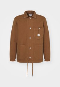 Brun knapplång jacka med elastiska ärmslut, tre framfickor, dragsko i nederkant och en liten vit Lee-logotyp på bröstfickan.