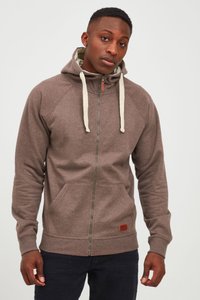 Sudadera con cremallera de tejido marrón con un acabado texturizado, que cuenta con una capucha, cordones de color crema, bolsillos frontales y un parche de logotipo de cuero.