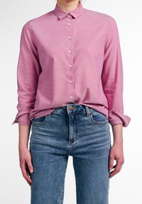 Růžová košile s dlouhým rukávem a límcem, vybavená strukturou látky a bílými knoflíky, v kombinaci s modrými džíny s vysokým pasem.