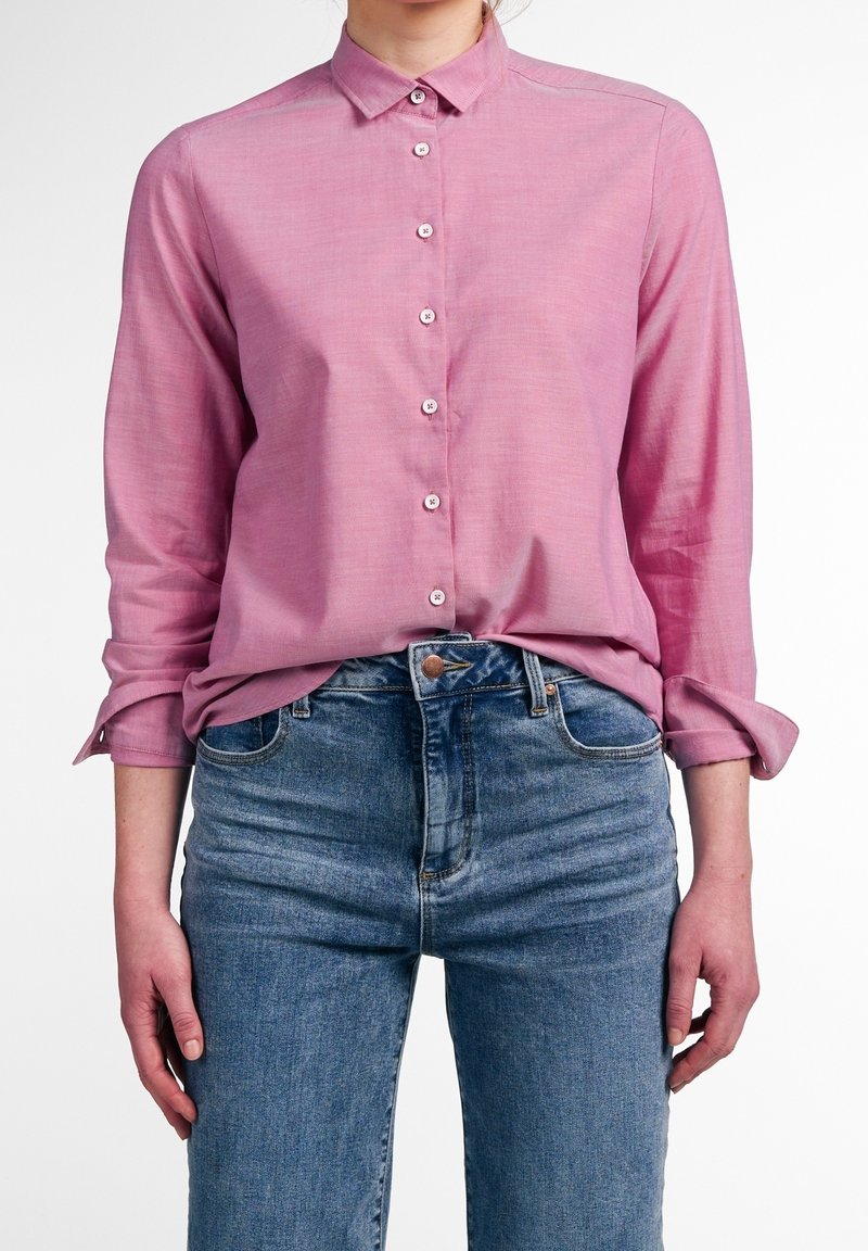 Růžová košile s dlouhým rukávem a límcem, vybavená strukturou látky a bílými knoflíky, v kombinaci s modrými džíny s vysokým pasem.