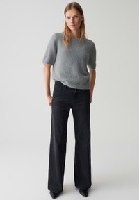 Grijze, kortarmige gebreide trui met een zachte textuur, gecombineerd met hooglopende zwarte flare jeans en pointed zwarte hakken. Eenvoudig ontwerp.