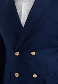 Blazer croisé bleu marine à finition satinée, avec des boutons dorés et une poche poitrine, au design ajusté et à la texture lisse.