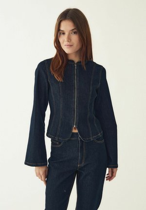 Donkere spijkerjasje met een aansluitend ontwerp, ritssluiting aan de voorkant en uitlopende lange mouwen. Contrasterende stiksels en een cropped lengte met afgeronde zoom.