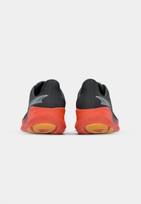 Chaussures de sport noires et oranges avec une semelle en caoutchouc texturée, un design de dos incurvé et un accent de logo réfléchissant sur le côté.