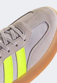 Gray suede sneaker with neon yellow stripes, featuring a smooth texture, lace-up design, and a brown rubber sole.