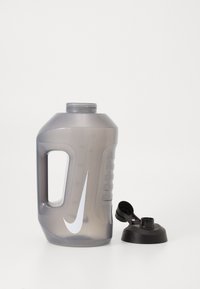 Grå plastvandsflaske med en struktureret greb, ergonomisk håndtag og en sort skruelåg. Har et fremtrædende hvidt logo på siden.