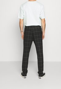 Svarta rutiga byxor med en figurnära design, som har gula rutor, en enda bakficka och kombineras med en ljus mintgrön t-shirt och sneakers.