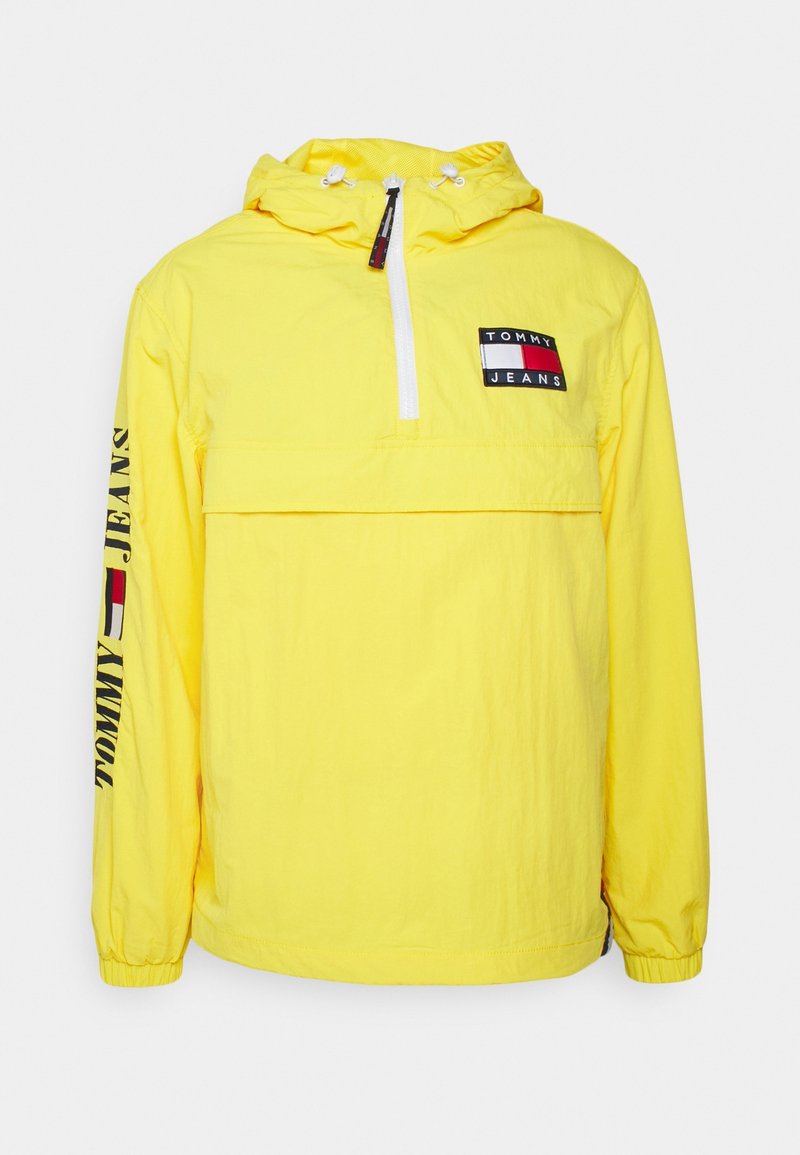 Giacca gialla con cappuccio realizzata in materiale leggero, dotata di una zip parziale frontale, tasca frontale e dettagli del logo su petto e manica.