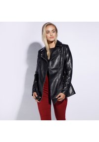 Black faux leather motorcycle jacket with diagonal zippers, lapels, and side accents. Model wears the jacket over red fitted pants.