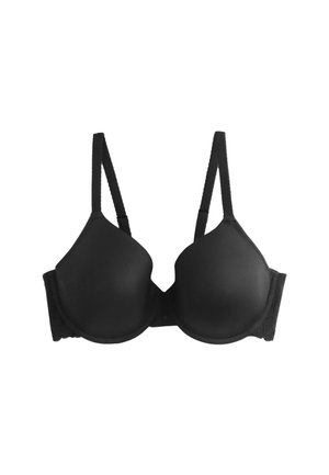 Közeli kép egy nőről, aki fekete alakformáló melltartót visel csipkedíszítéssel az elülső középen, kivillan a kivágás és a sima anyagtextúra.