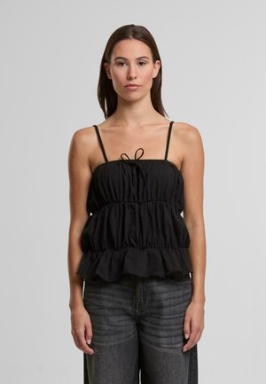 Čierny peplum top s nastaviteľnými špagetovými ramienkami, zberanou textúrou, viacvrstvovým volánovým lemom a predným mašľovým detailom. Nosí sa s sivými džínsami.