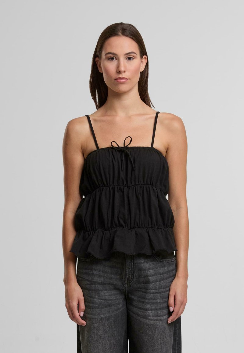 Top en peplum noir avec des bretelles spaghetti ajustables, texture froncée, ourlet volangé à plusieurs niveaux et un détail avec un nœud à l'avant. Porté avec un jean en denim gris.