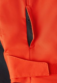 Oranje stoffen reddingsvest met een ritssluitingszak, gestikte accenten en een band. Het materiaal lijkt textuur te hebben en duurzaam te zijn.