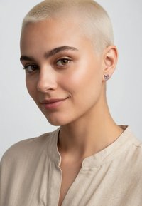 Fjärilsörhängen med flerfärgade accenter, infattade i silver, bärs av en modell i en beige, texturerad topp med hög halsringning.