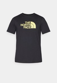 Černé tričko s krátkým rukávem vyrobené z měkkého materiálu, s velkým žlutým logem "THE NORTH FACE" přes hrudník.