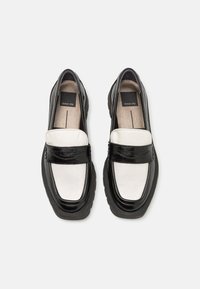 Black and white loafers with a smooth leather upper, featuring a contrasting textured strap, rounded toe, and thick rubber sole.