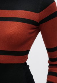 Haut en maille noir à rayures rouille, présentant une texture côtelée, une coupe ajustée et des rayures horizontales proéminentes de différentes largeurs.