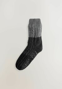 Strikket grå og sort sok med strukturerede mønstre og en ribbet manchet. Sorte skridsikre prikker på sålen for bedre greb.