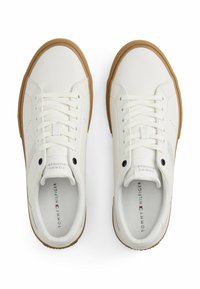 Zapatillas de piel blanca con una suela de goma texturizada. Las características incluyen cordones blancos, un logo sutil y costuras de color claro.