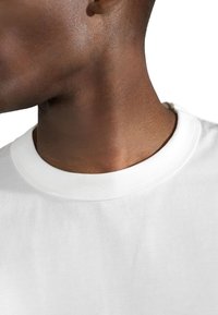 Vitt bomullströja med rund halsringning, med en mjuk textur och korta ärmar, som visar en närbild av krageområdet och nacken.