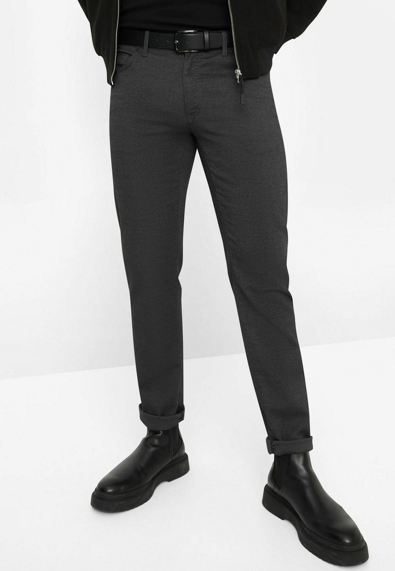 Grijze slim-fit broek van textuurstof, met een opgerolde zoom, gedragen met een zwarte riem en leren enkellaarsjes.