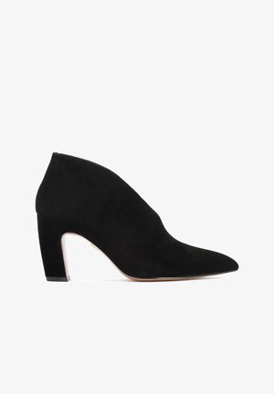 Musta sametist pahkluudega saapad, millel on terav nina, sile tekstuur ja jämedam konts. Erakordne külje lõike detail täiustab disaini.