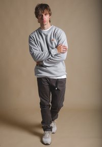 Sudadera gris con logo de oso bordado, combinada con pantalones oscuros y zapatillas claras. Textura suave y ajuste relajado en todo el conjunto.