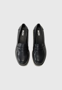 Mocassins de pele preta com um acabamento suave, apresentando um topo cosido e uma faixa curva na parte superior. Por dentro, exibe a marca "KOI".